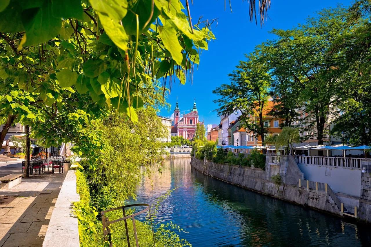 River flowing through Ljubljana with pink Franciscan Church and lush spring foliage.