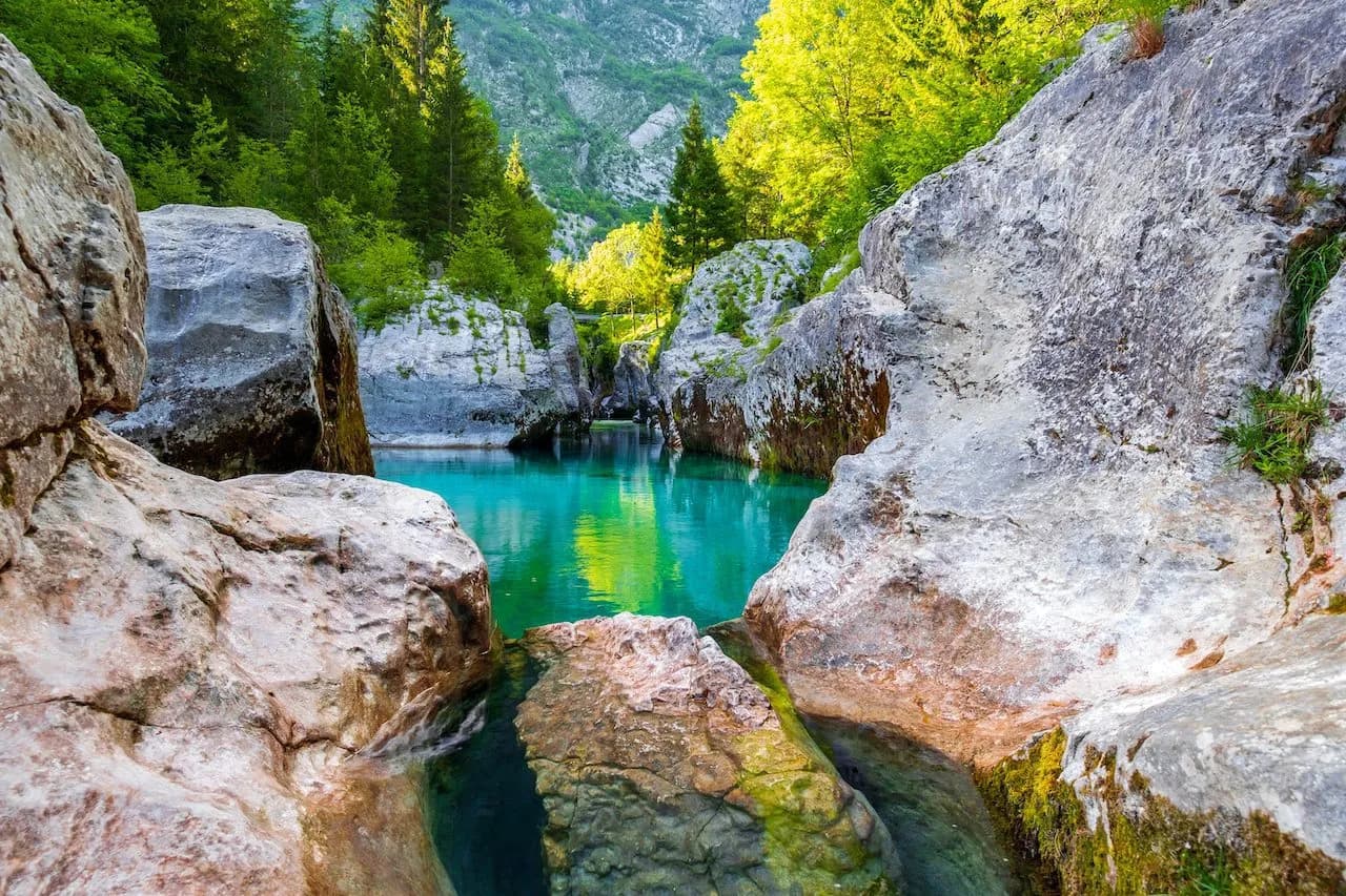Turquoise water flowing through a gorge with large rocks and green forest in the Great Gorge of Soca.