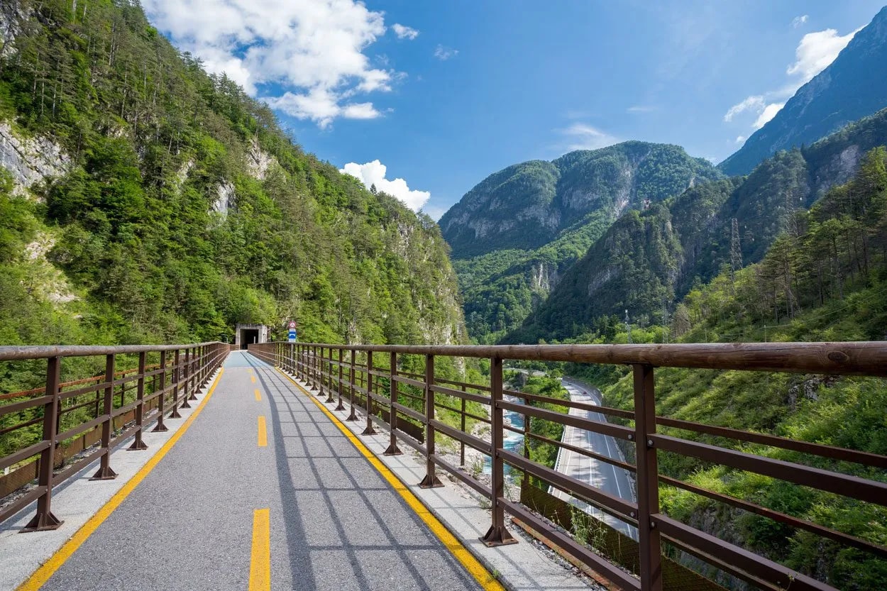 Cycling path on bridge leading to a tunnel through lush green mountains in Val Canale.