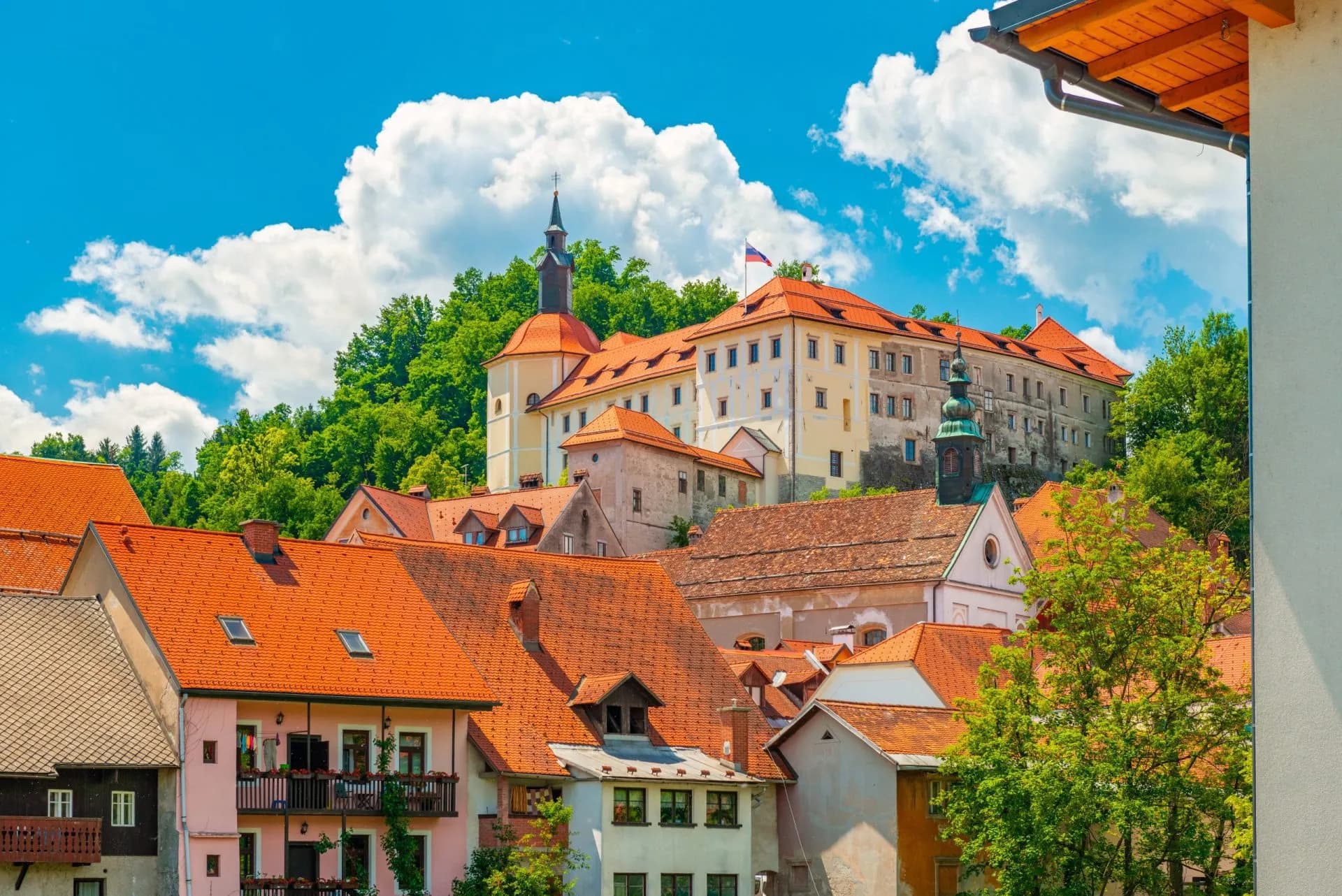 Historic town of Škofja Loka with red roofs and castle on a green hill under blue sky.