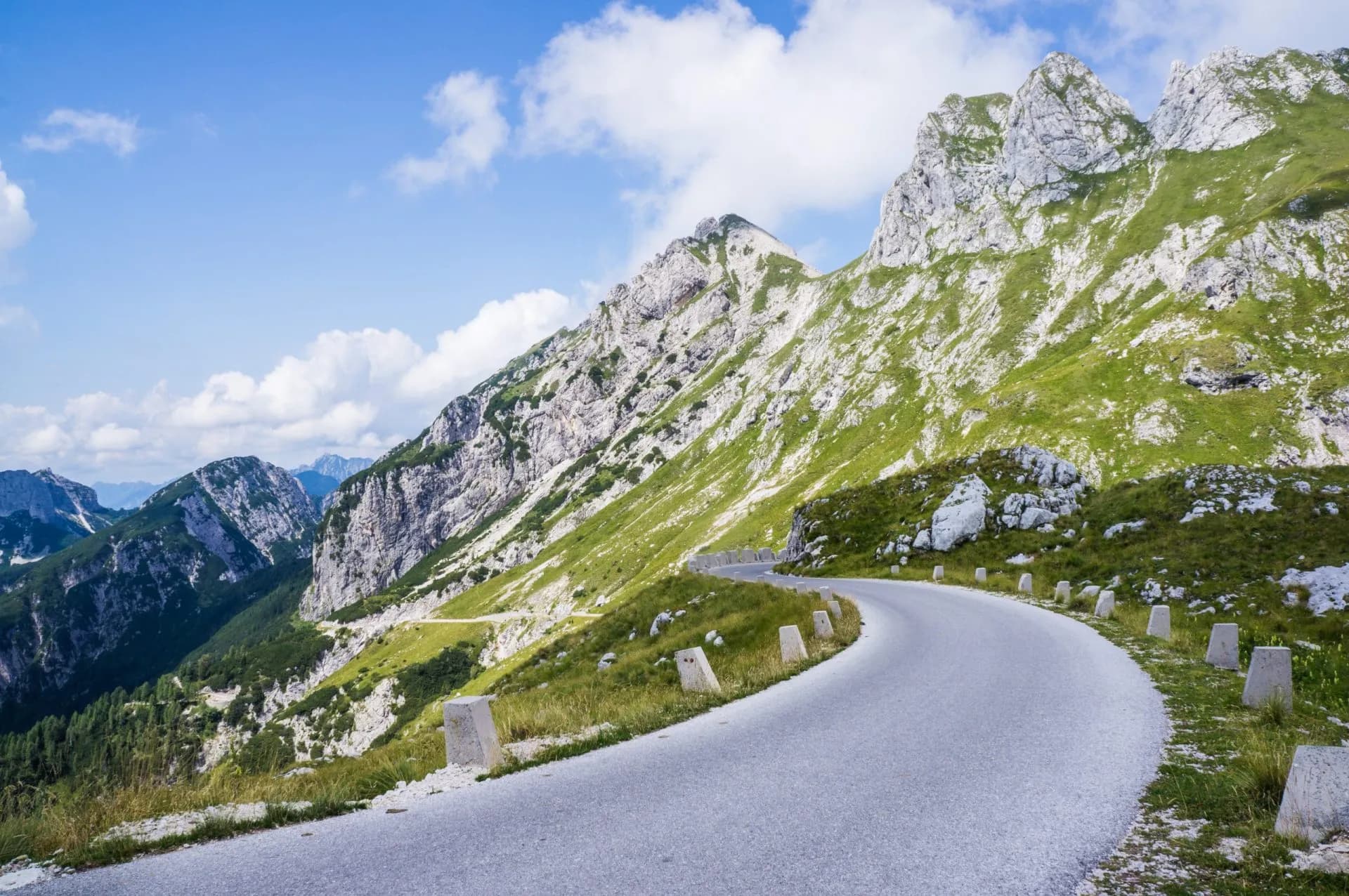 Winding mountain road ascending steep green slopes toward Mangart Saddle in Slovenia