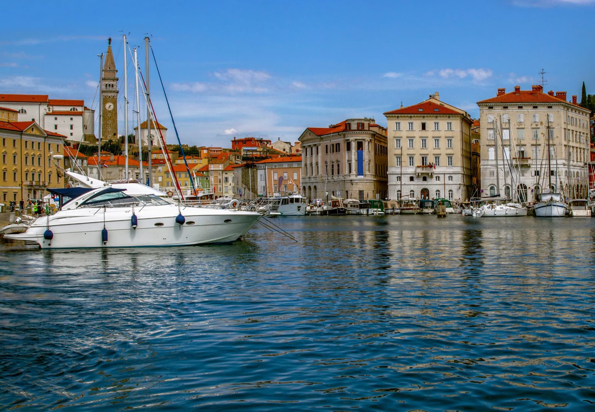 White motor yacht docked in harbor with historic coastal town and bell tower background.