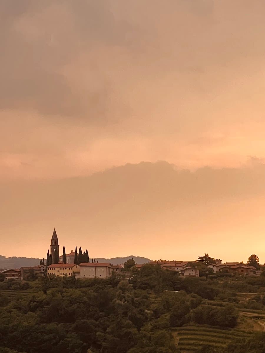 Hilltop village with tall church steeple above dark green trees at sunset