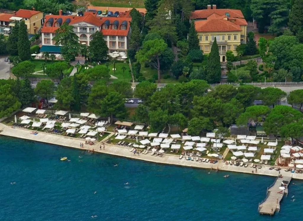 Hotel Marko beach area with lounge chairs, umbrellas, and people swimming in blue coastal water.