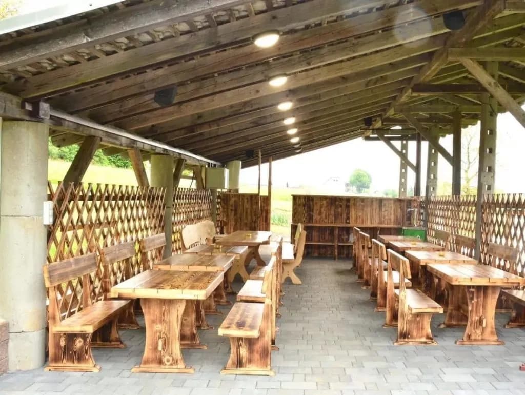 Outdoor seating area with rustic wooden tables and benches under a covered patio at Glamping Zgornja Dobrava.