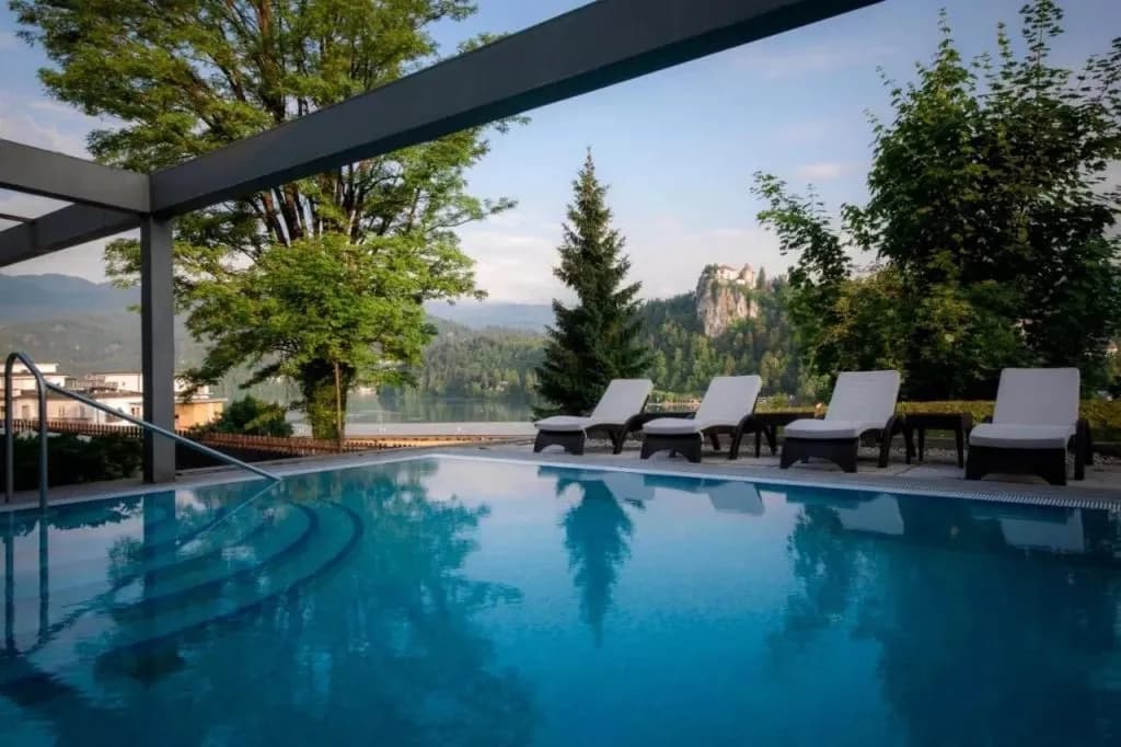 Outdoor pool with lounge chairs overlooking Lake Bled and Bled Castle on a cliff.