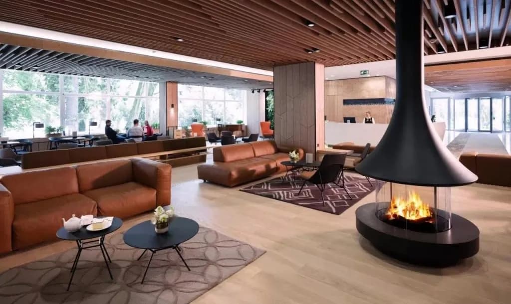 Modern hotel lobby with brown leather sofas, wood ceiling, and central hanging fireplace.