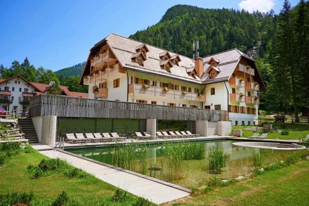 Hotel Plesnik building with balconies, natural swimming pool, and forested mountain backdrop.