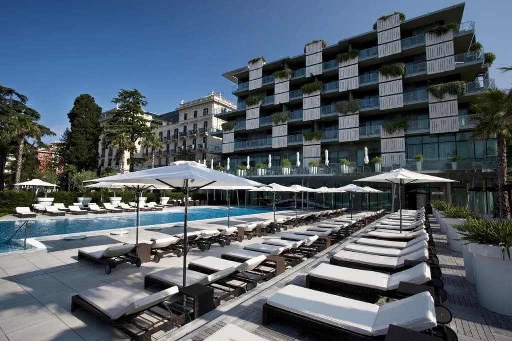 Hotel Kempinski Palace pool area with rows of lounge chairs and white umbrellas under a clear blue sky.