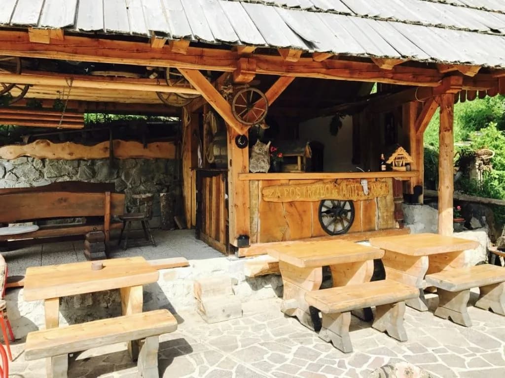 Outdoor rustic wooden seating area next to a log cabin bar structure in Petrovo Brdo.
