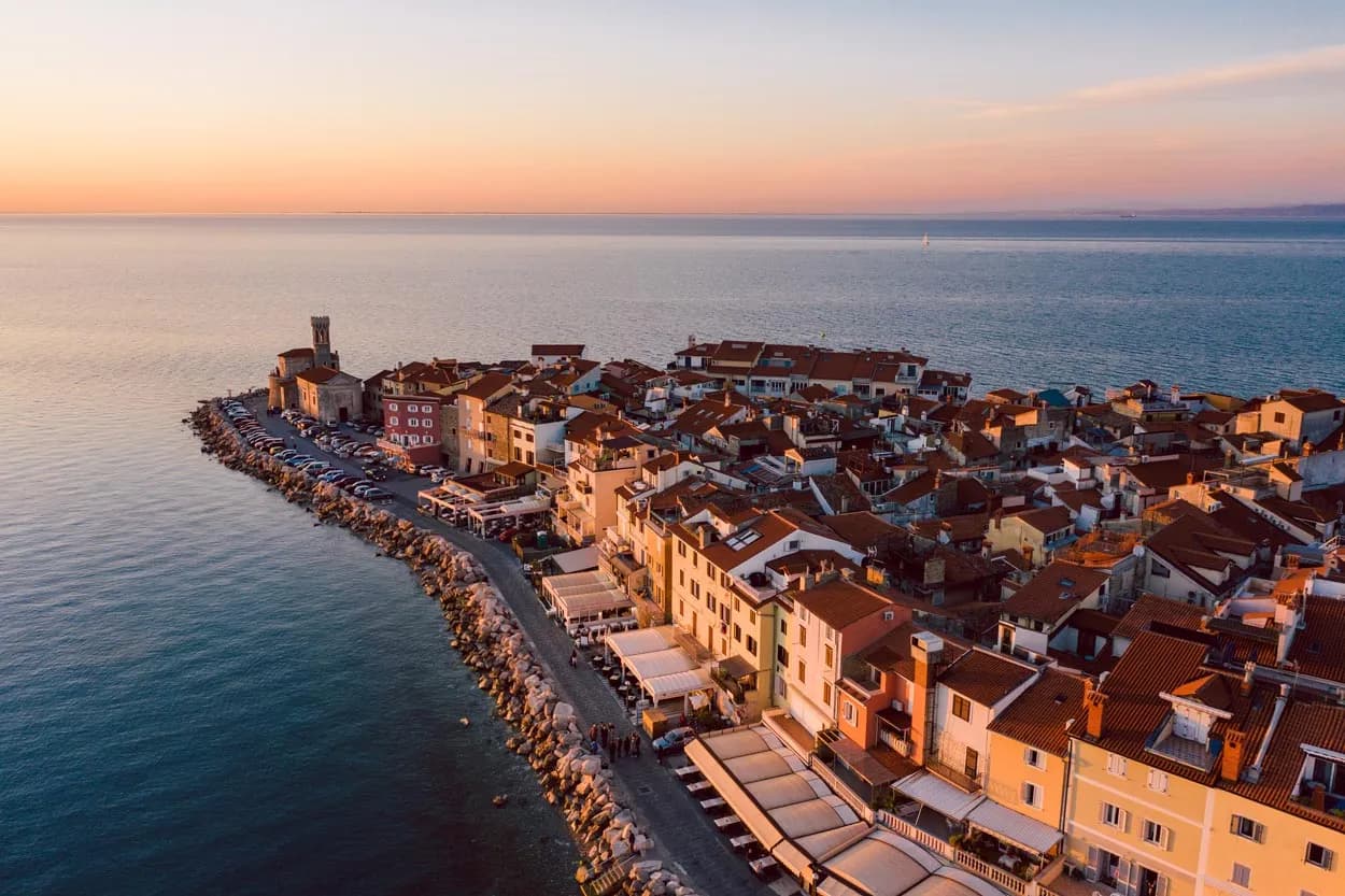 Panoramic view of Piran coastal town with terracotta roofs at sunset over the sea.