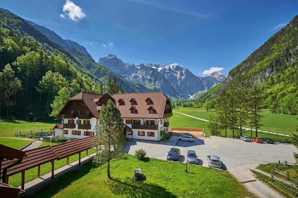 Alpine hotel with brown roof nestled in a green valley with snow-capped mountains