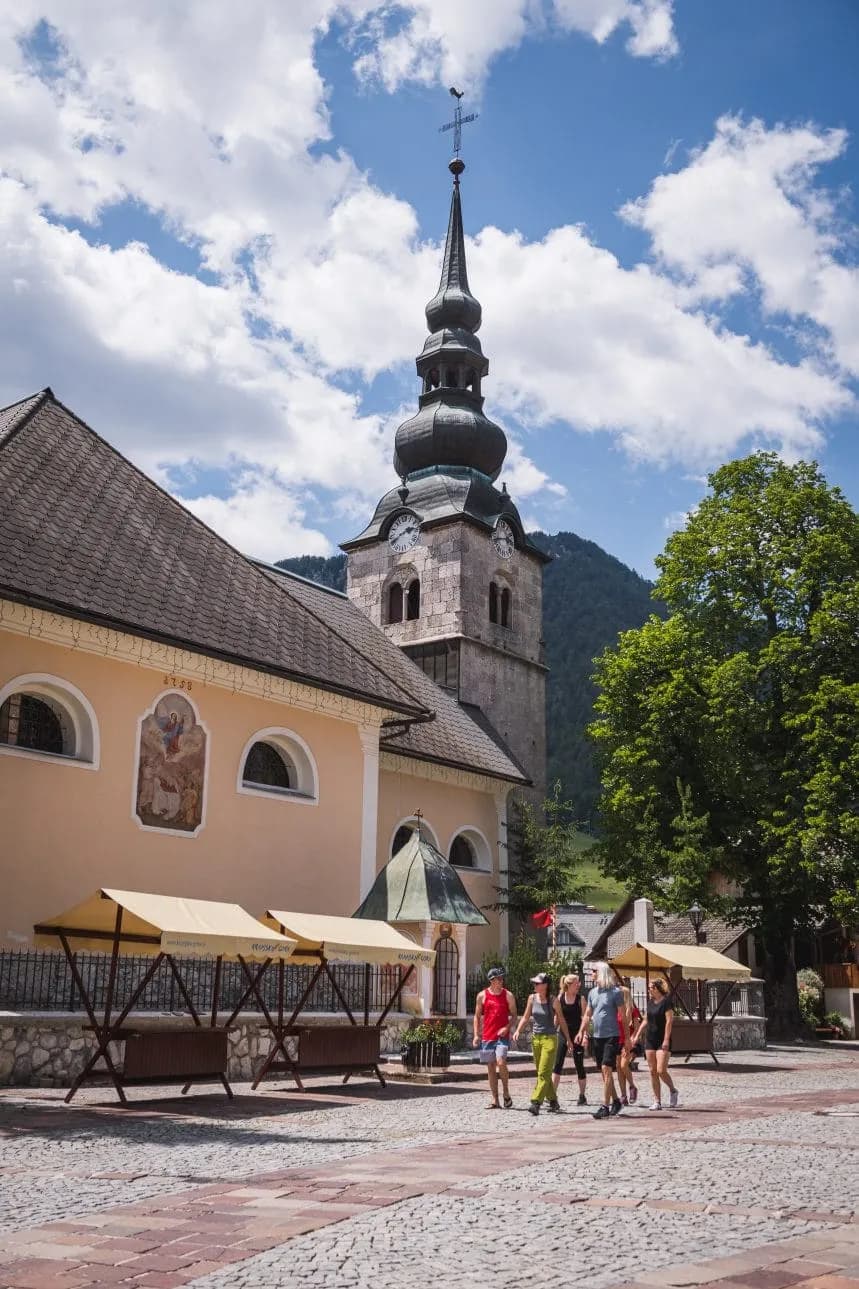 Church tower and market stalls on the main square in Kranjska Gora under a blue sky.