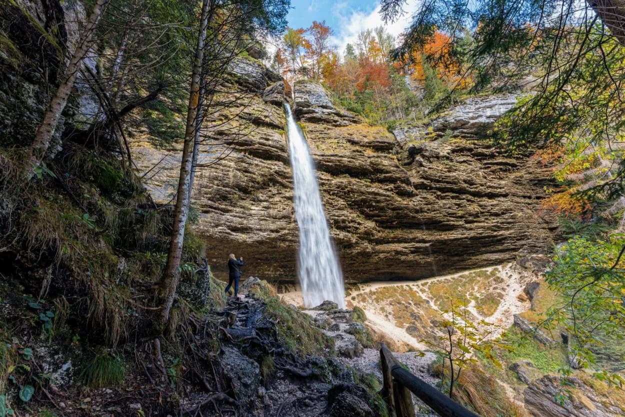 Tall waterfall cascading down layered rock face with autumn foliage, Pericnik Waterfall, Slovenia