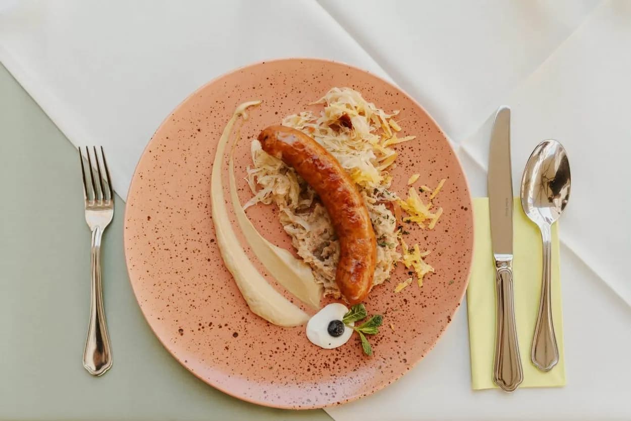 Grilled sausage with sauerkraut and sauce served on a pink speckled plate with silverware.