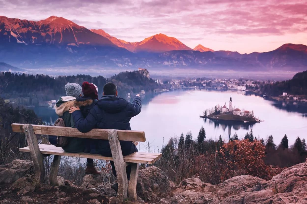 Couple watching sunset over Lake Bled island church and mountains from viewpoint bench
