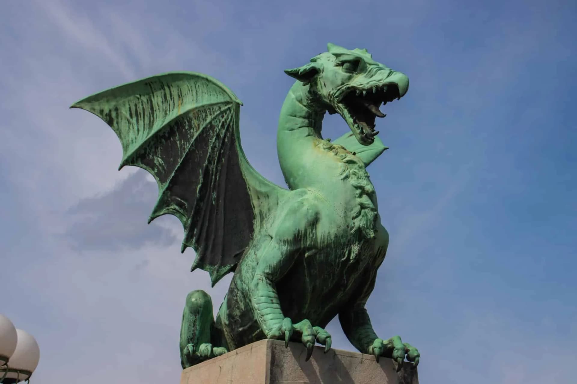 Verdigris dragon statue with wings spread against a blue sky at Ljubljana Dragon Bridge.