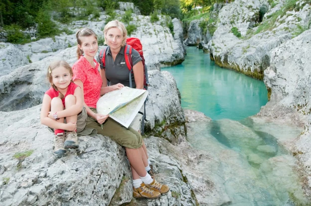 Hikers with map resting by turquoise river flowing through rocky gorge, Soca River