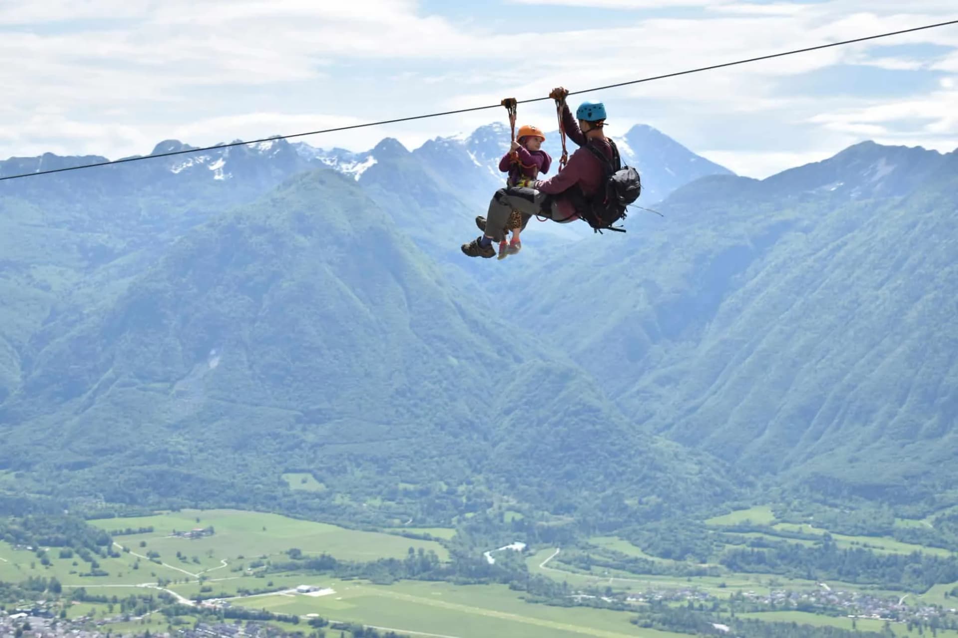 Father and child ziplining high above a green valley with forested mountains in Bovec.