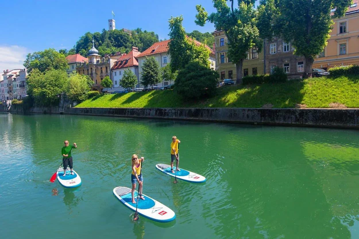 Stand-up paddling on the green Ljubljanica River with Ljubljana Castle in the background.