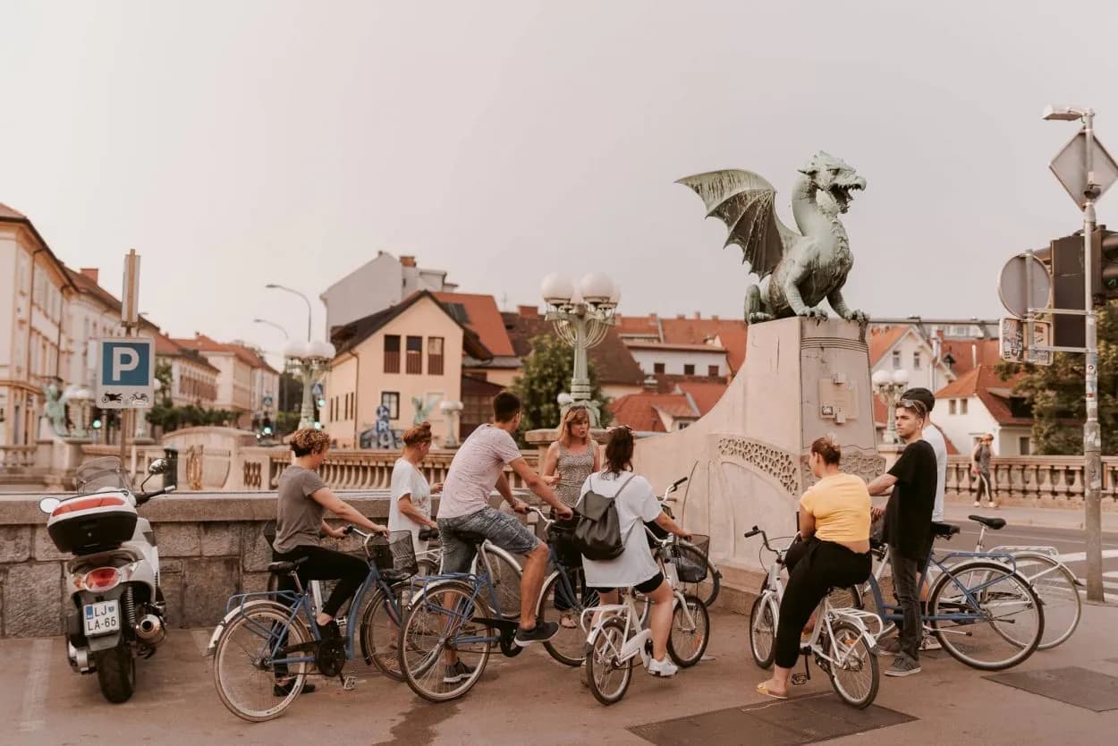 Bicycle tour group near Ljubljana Dragon Bridge with a bronze dragon statue visible.