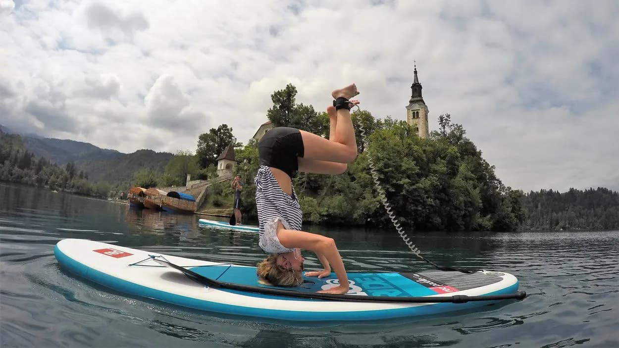 Paddleboarding headstand on Lake Bled with church tower visible in background