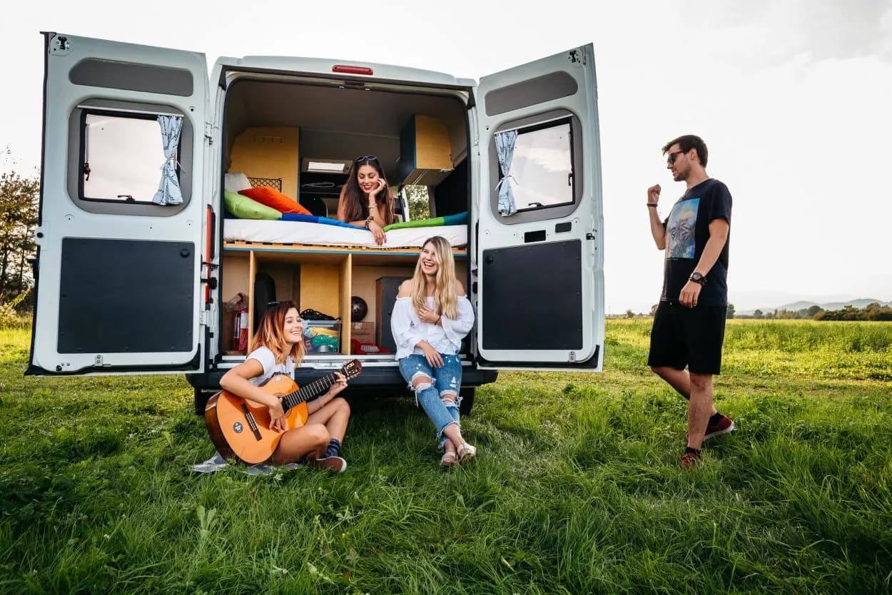 Campers relaxing by open camper van with guitar music in grassy field
