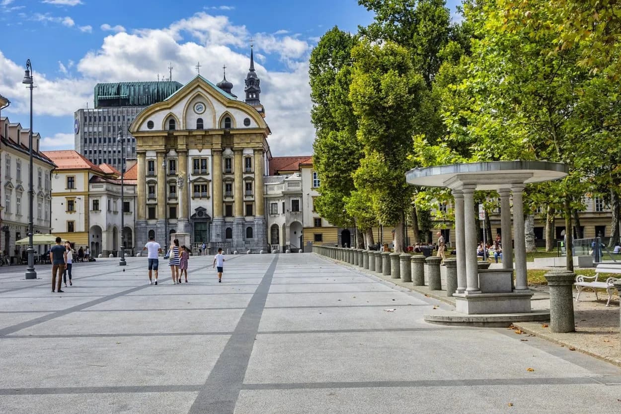 People walking across Kongresni trg square toward the Ursuline Church in Ljubljana.