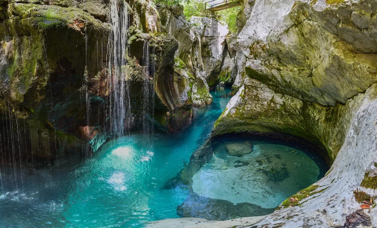 Canyoning in a gorge with turquoise water, small waterfalls, and mossy rock walls.
