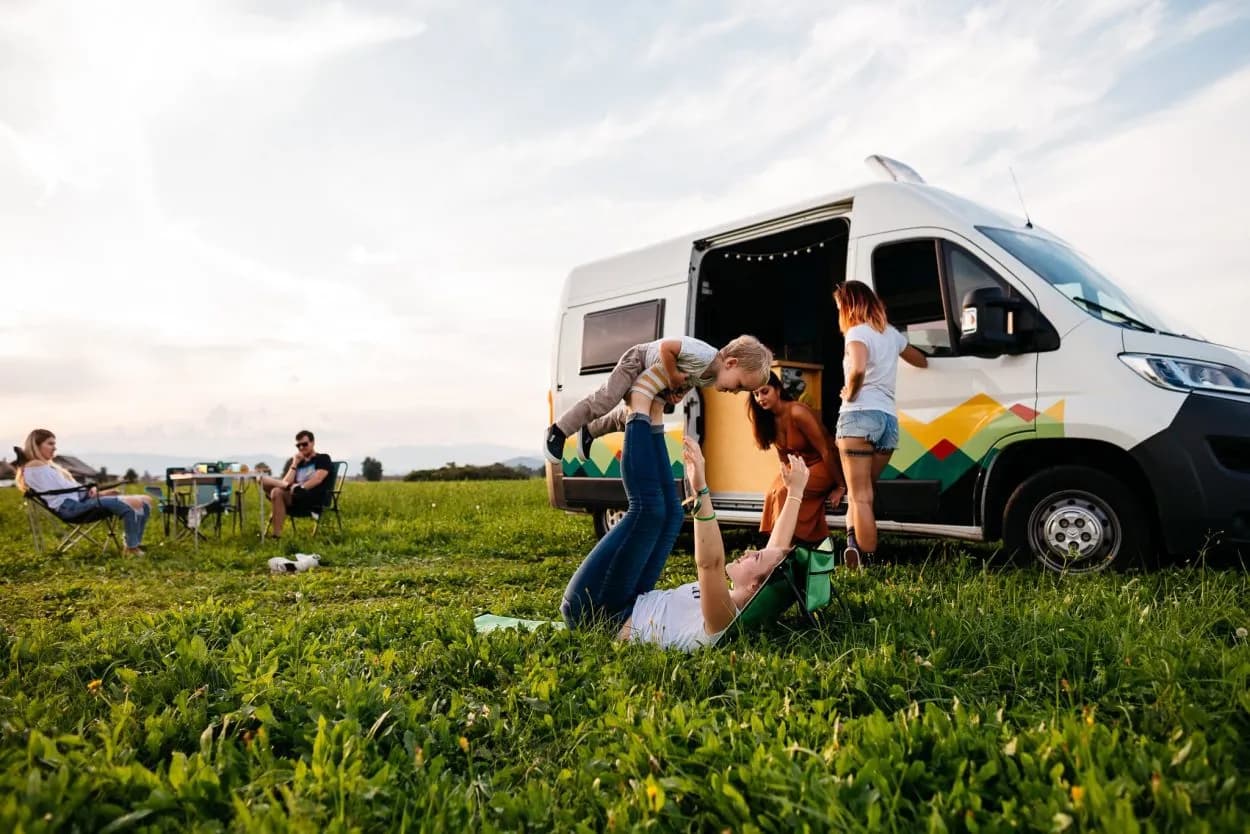 Family camping with camper van enjoying playtime in grassy field at sunset