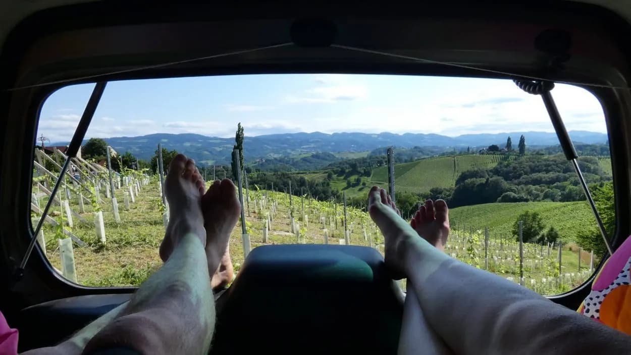 Feet resting while viewing rolling green vineyards and distant hills from a vehicle.
