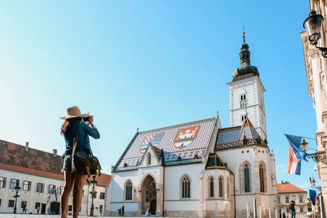 Tourist photographing St. Mark's Church with colorful tiled roof in Zagreb old town.