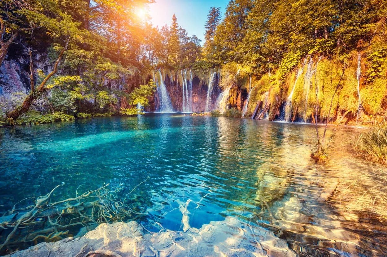 Plitvice Lakes waterfalls cascading into turquoise pool with sunlit autumn foliage