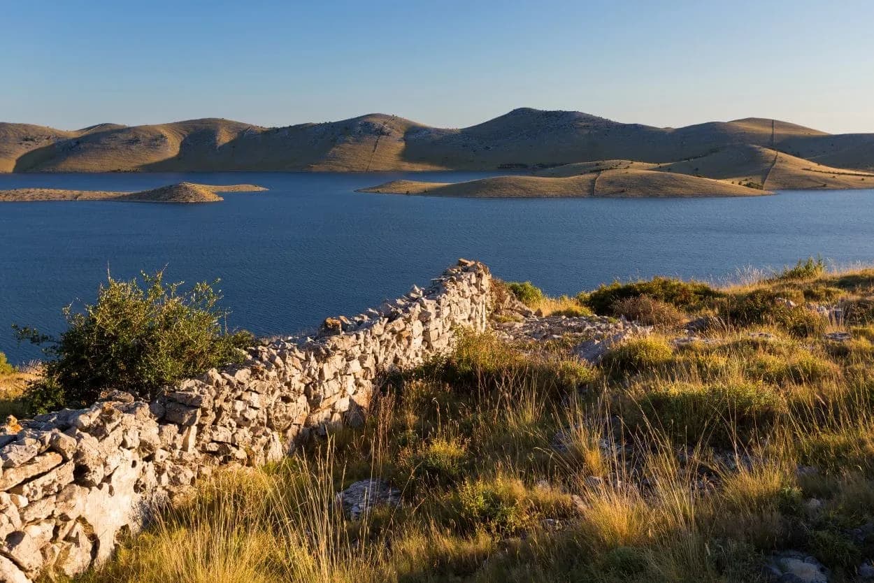 Stone wall overlooking blue water, small islands, and arid hills in Kornati National Park.