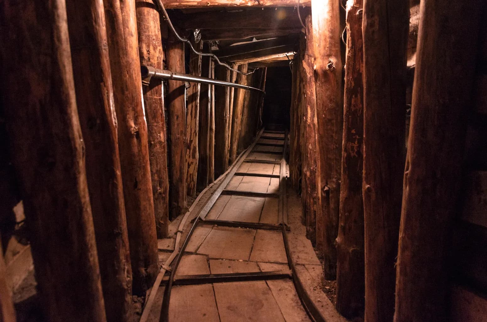 Narrow tunnel interior supported by rough wooden logs with a wooden walkway and metal rail in Sarajevo.
