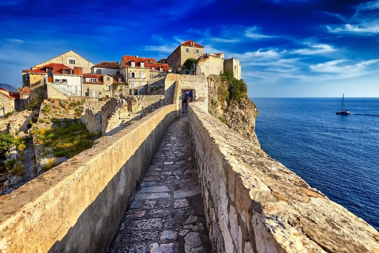 Stone walkway on Walls of Dubrovnik overlooking blue Adriatic Sea with sailboat.