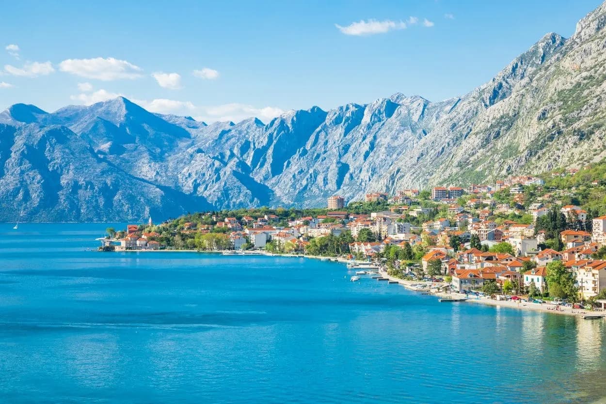 Coastal town with red-roofed buildings nestled below steep mountains on the Bay of Kotor.