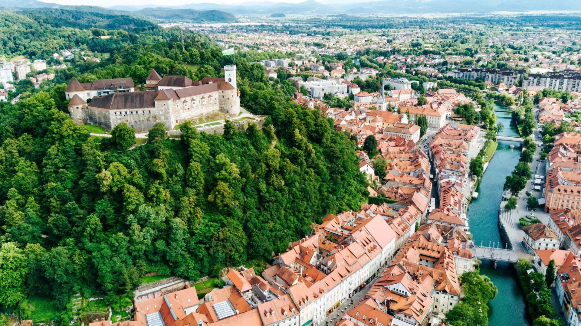 Ljubljana Castle overlooking the city center and Ljubljanica River with red rooftops.