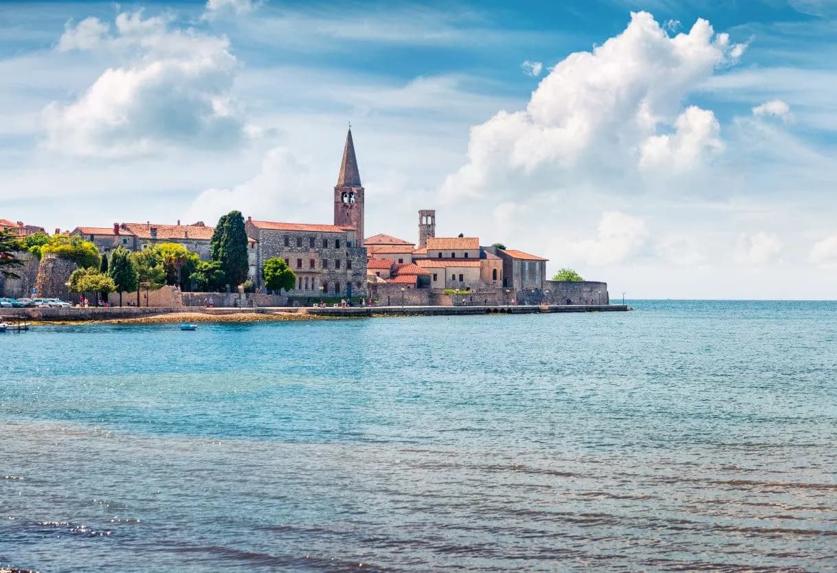 Coastal view of Poreč town with stone buildings and a tall bell tower overlooking the Adriatic Sea.