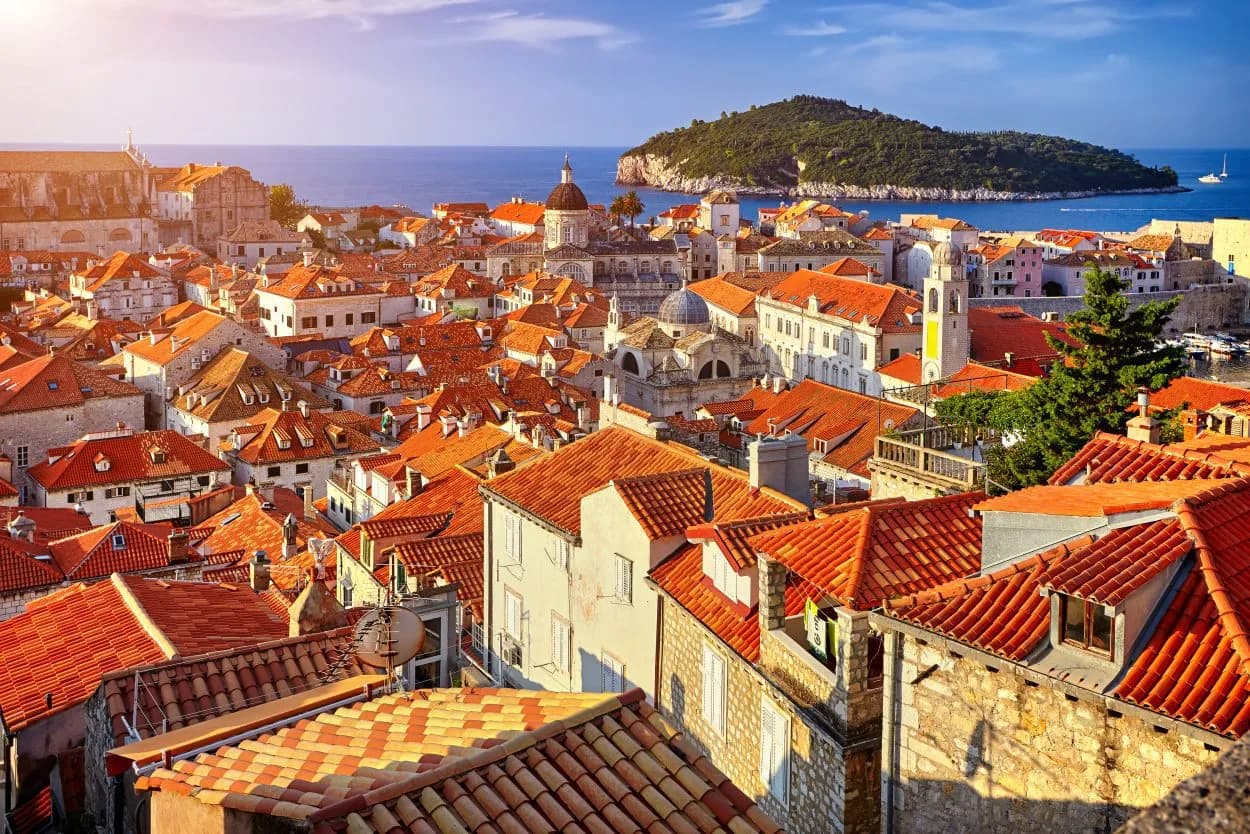 Rooftops of Dubrovnik with orange tiles, blue sea, and Lokrum Island in the background.