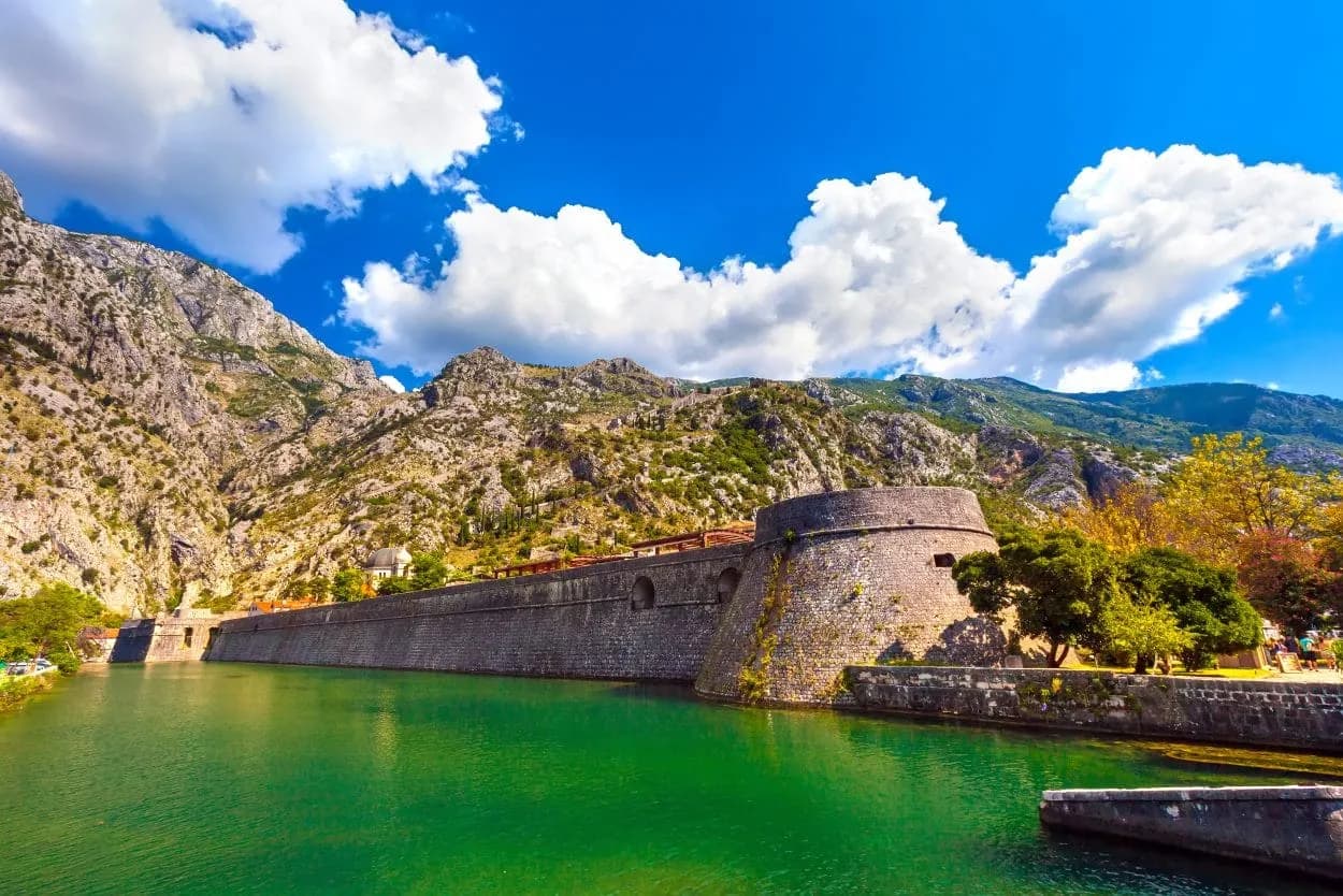 Kotor town fort wall beside emerald water with steep mountains under blue sky