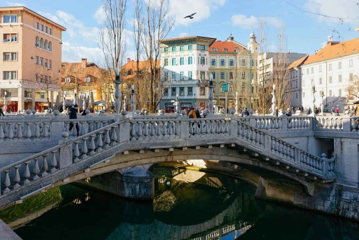 Stone bridge with balustrade over dark water in a European city square.
