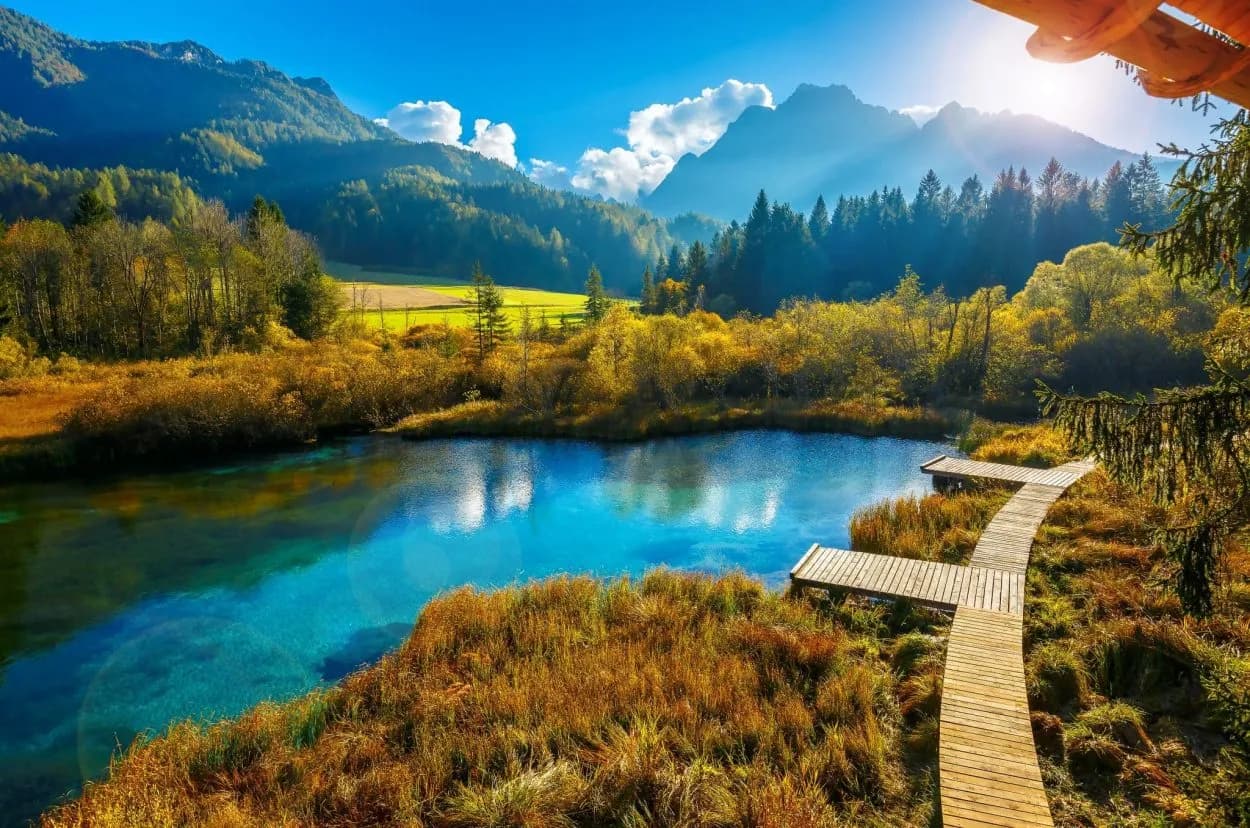 Wooden boardwalk next to bright blue water in Zelenci Nature Reserve with mountains.