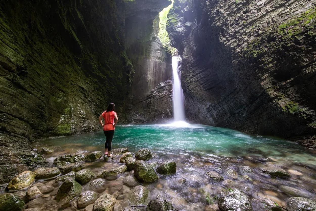 Waterfall Kozjak plunging into turquoise pool inside a mossy canyon with a person observing.