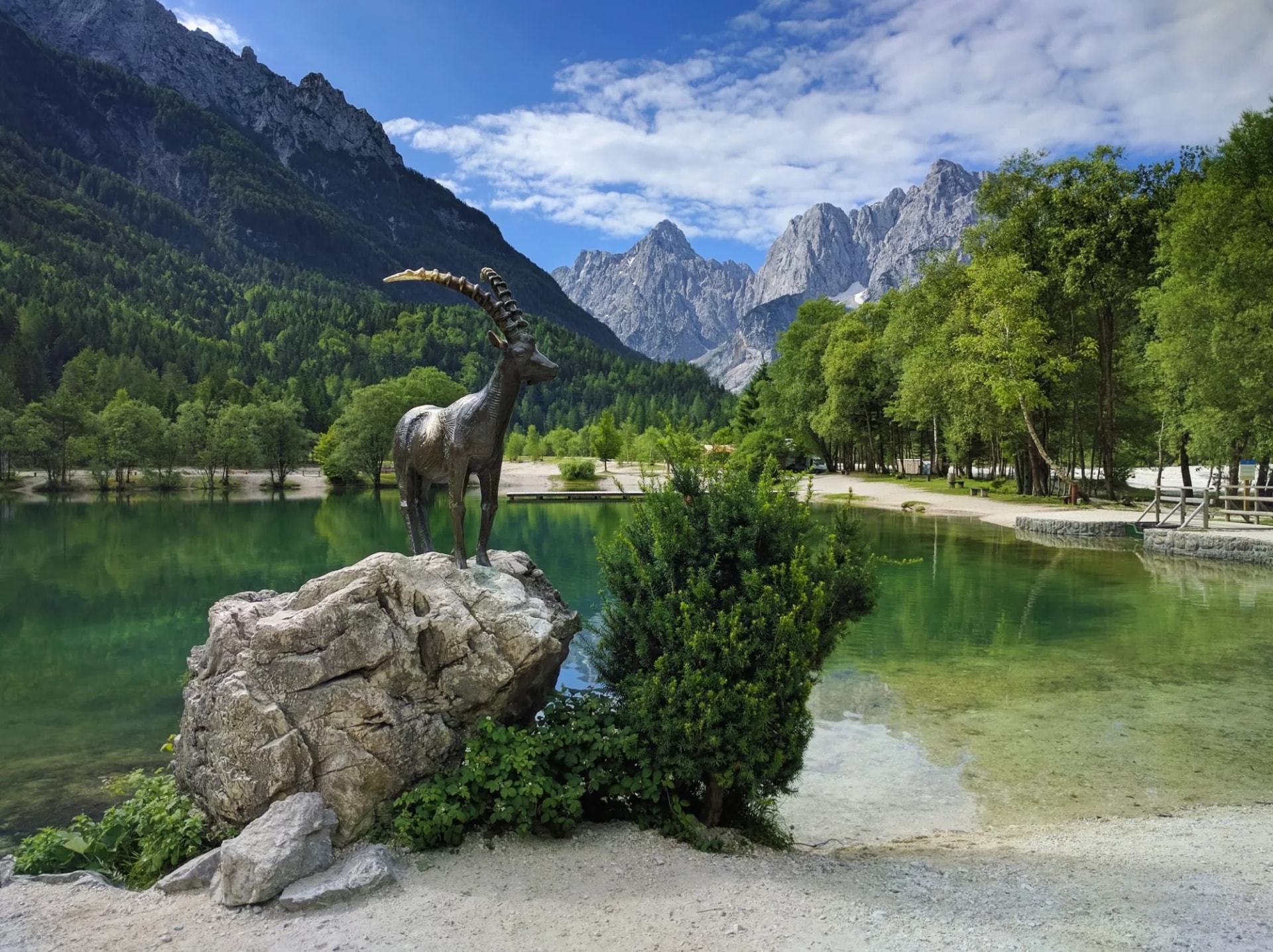 Mountain goat statue by Lake Jasna with green water and Julian Alps in Kranjska Gora.