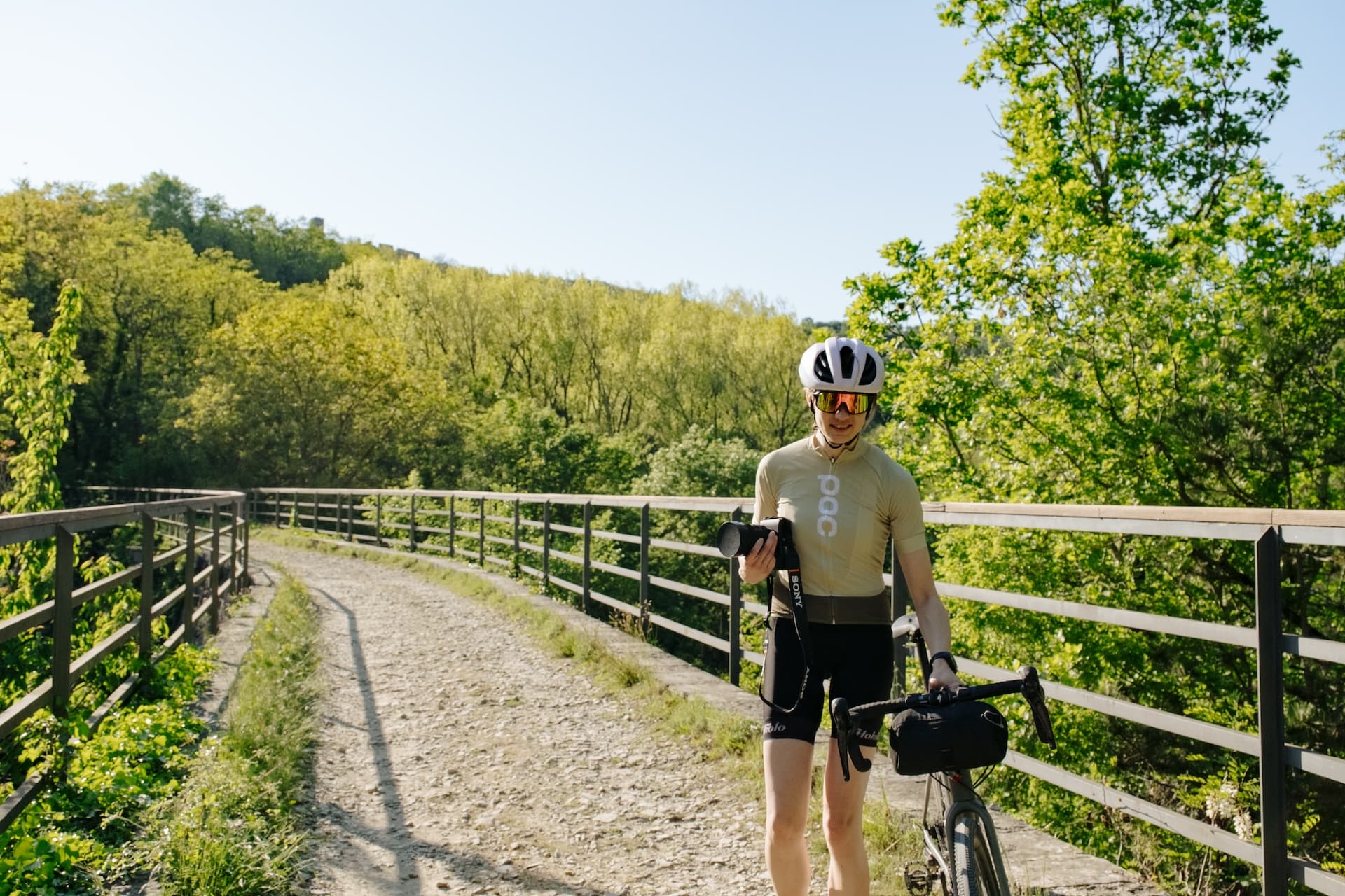 Cyclist walking on Parenzana bridge with gravel path and lush green forest.