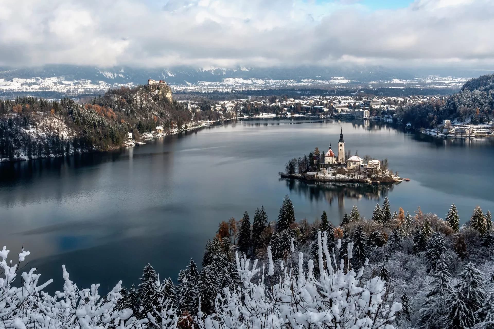 View of Lake Bled with island church and castle on snowy hills in winter.