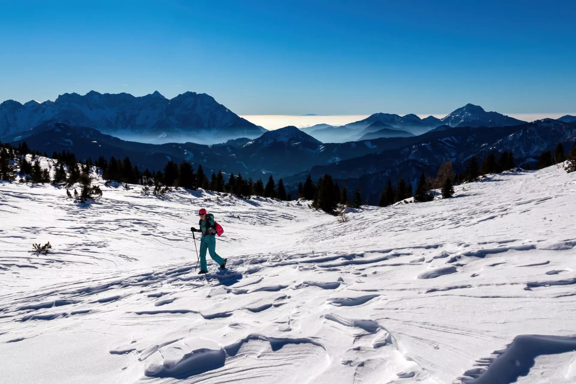 Snowshoeing in winter mountains with layered blue peaks and a clear sky.