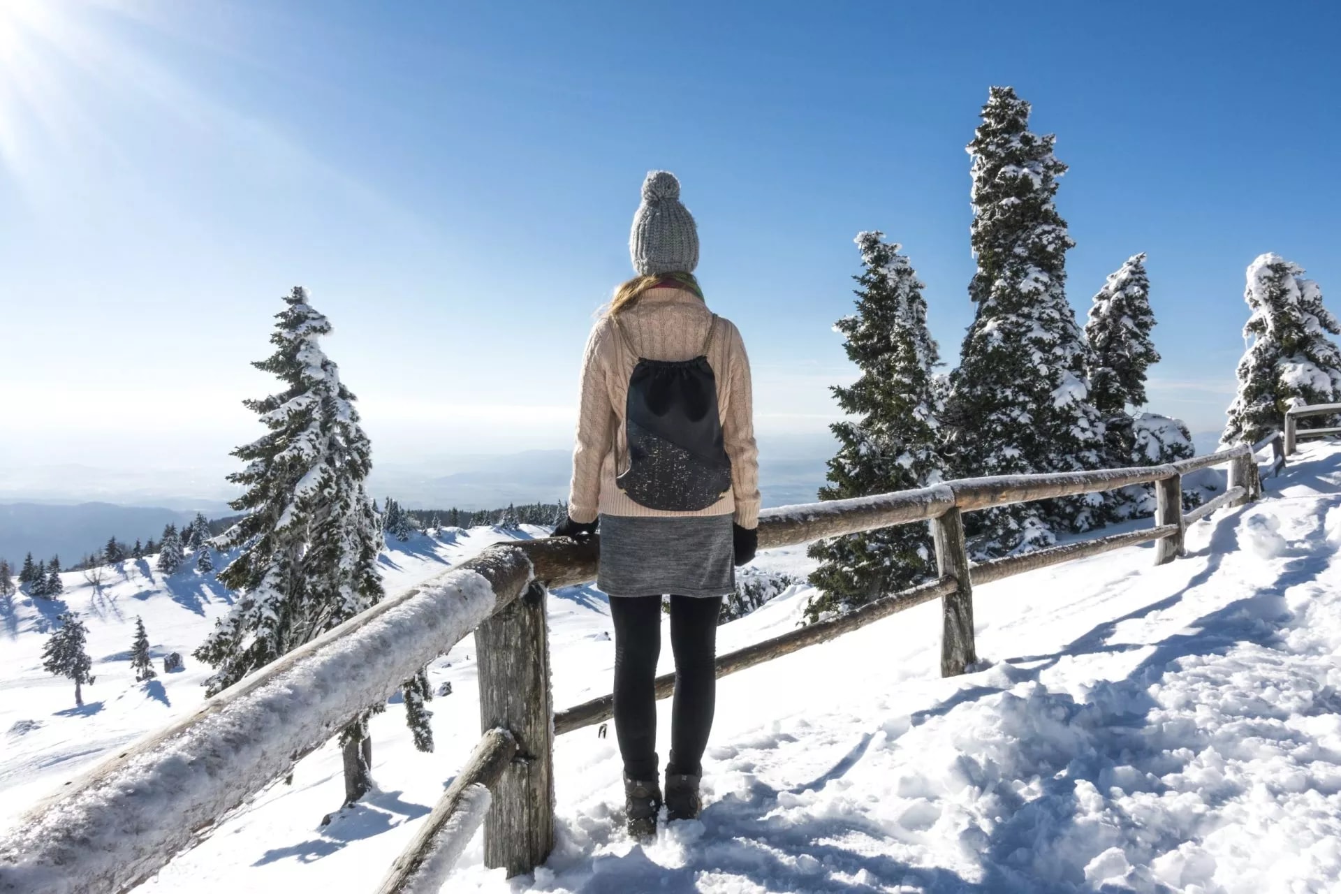 Winter hiking in Slovenia: Person with backpack views snowy alpine landscape and sunlit peaks.