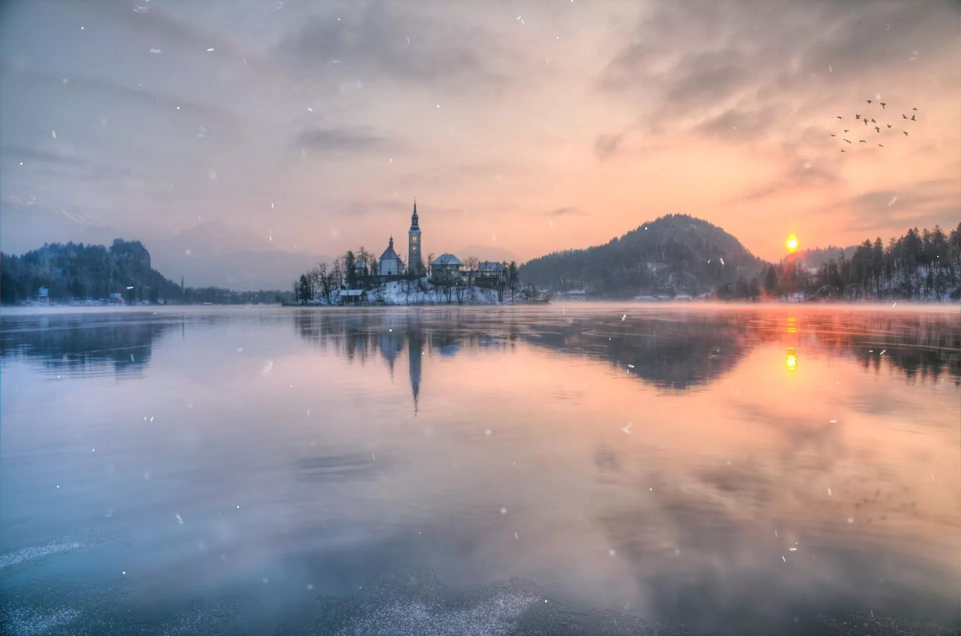 Winter sunrise at Lake Bled with snow falling on the partially frozen water.